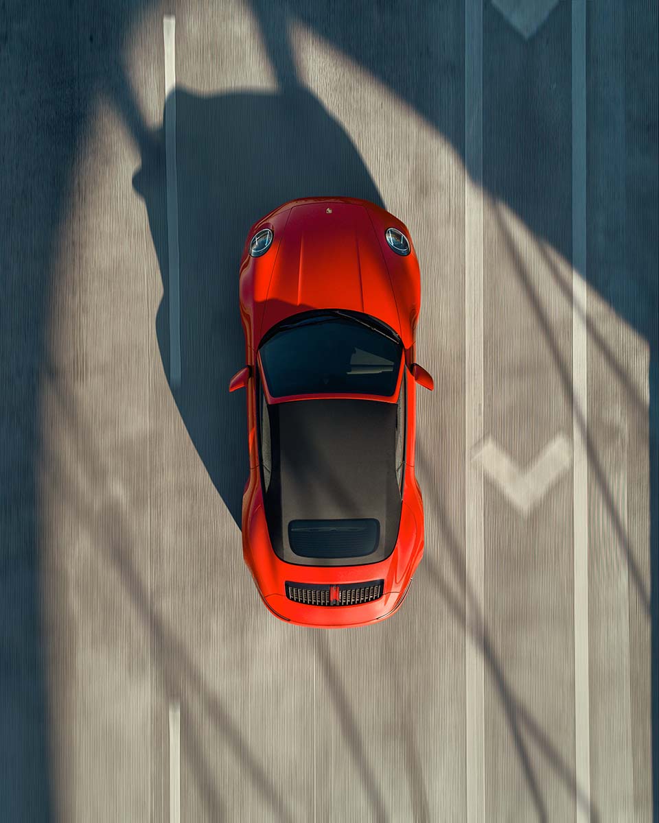Top-down aerial of a red Porsche 911 Carrera casting long shadows across the pavement, by Niaz Uddin