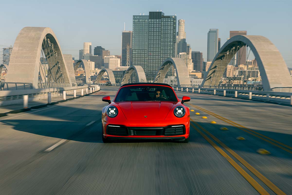 Red Porsche 911 Carrera cabriolet driving under the 6th Street Bridge arch in golden-hour light, by Niaz Uddin