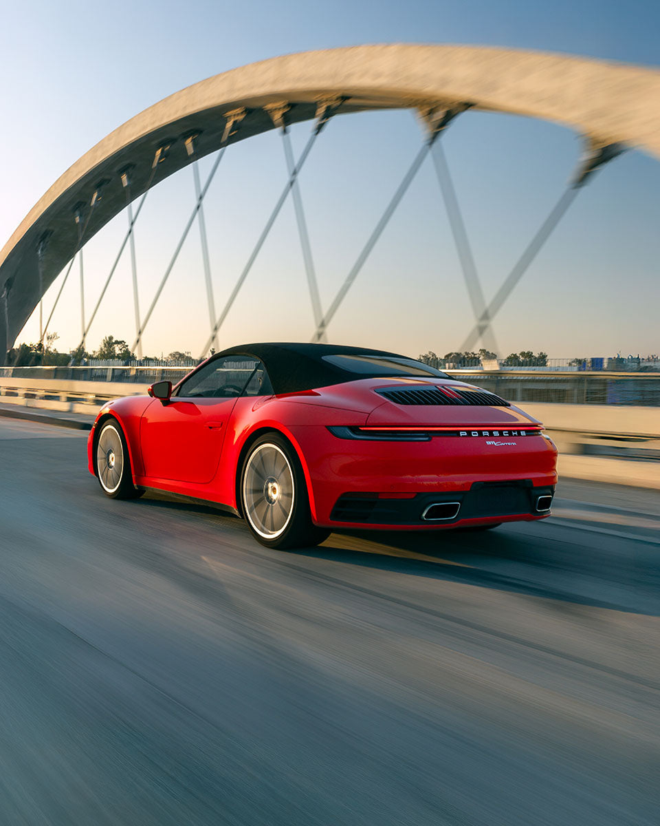Rear three-quarter of a red Porsche 911 Carrera cabriolet in motion under the arch of the 6th Street Bridge, by Niaz Uddin