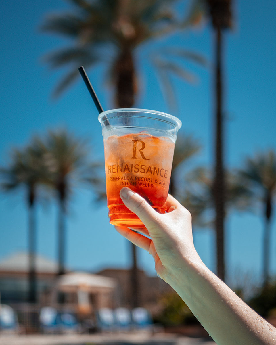 Hand holding a Renaissance Esmeralda signature cocktail under the palms in Indian Wells