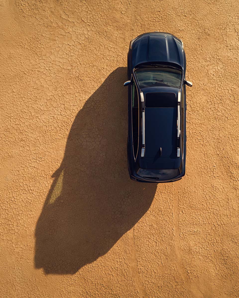 Top-down aerial of a blue Subaru Outback casting a long shadow on cracked desert ground, by Niaz Uddin