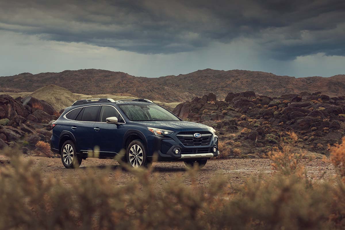 Blue Subaru Outback on open desert at sunset, front three-quarter view, by Niaz Uddin