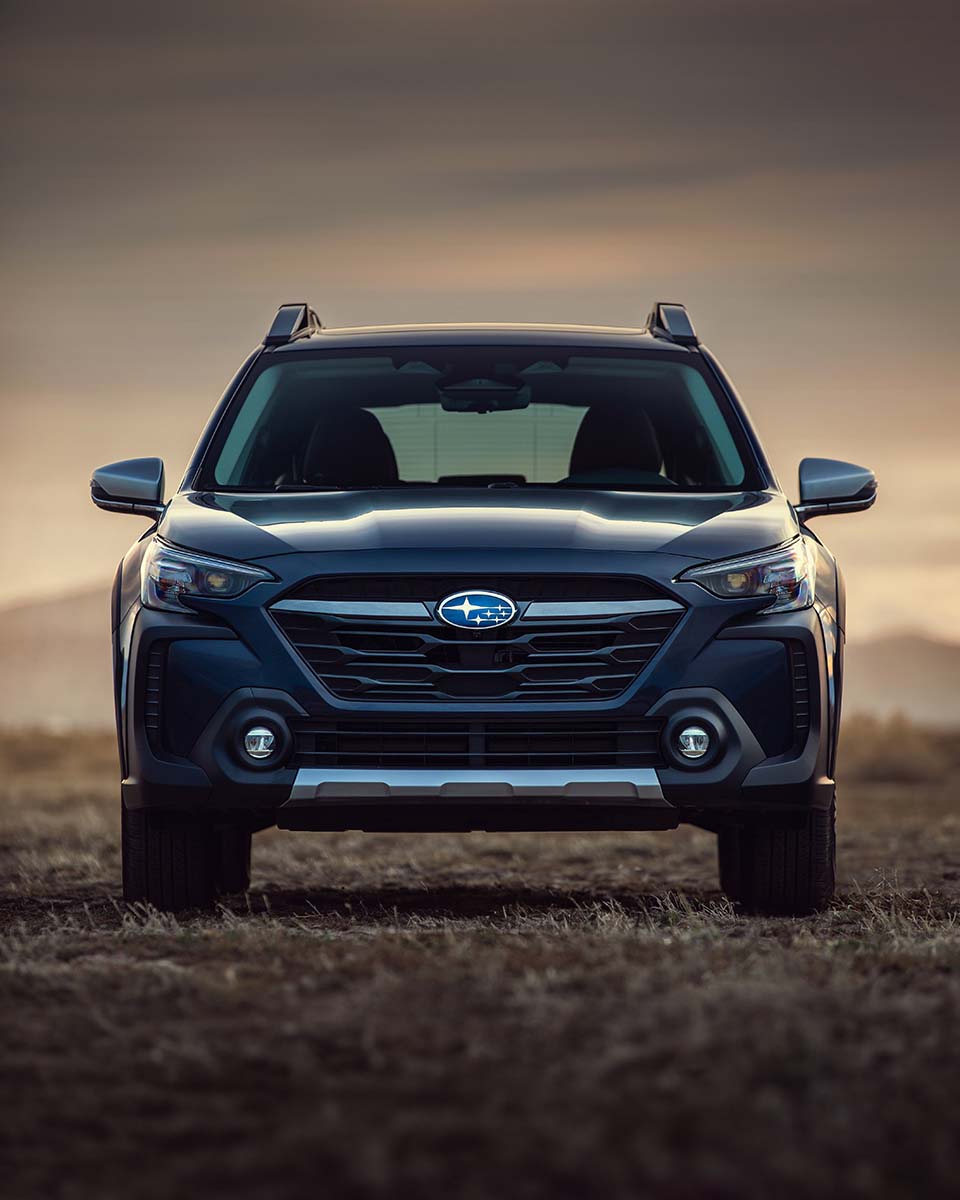 Front grille of a blue Subaru Outback on a hilltop at golden hour, by Niaz Uddin