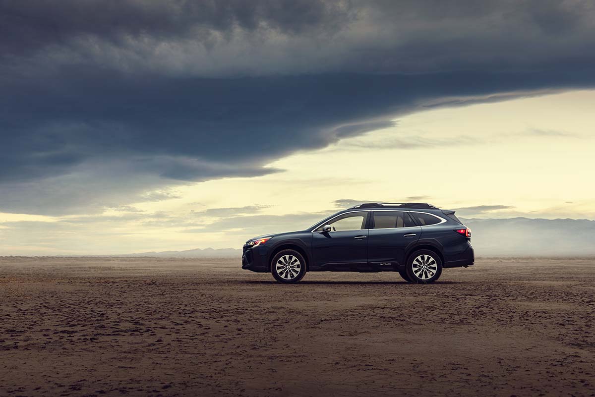 Blue Subaru Outback side profile in the desert under dramatic clouds, by Niaz Uddin